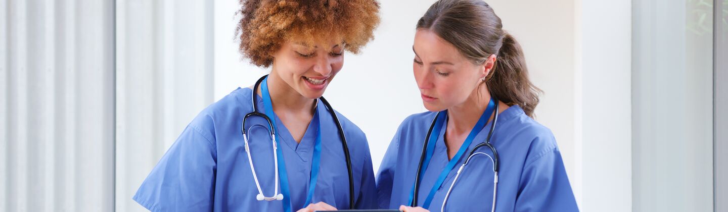 COLOUR-IMAGE_two-female-nurses-using-tablet-wearing-blue-scrubs_apr26