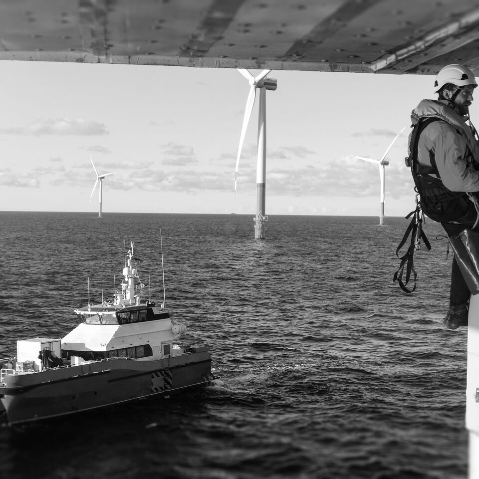 SINGLE-IMAGE_worker-on-wind-turbine-with-boat-in-distance-black-and-white_jul24